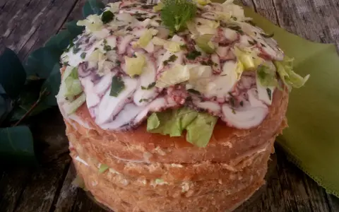Panettone Gastronomico with sliced octopus, lettuce, and herbs on a wooden table.