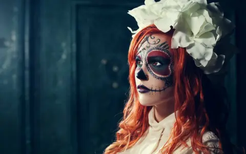 Kvinna med detaljerad ansiktsmålning för halloween, klädd i en vit blus och med en stor blomsterkrans.