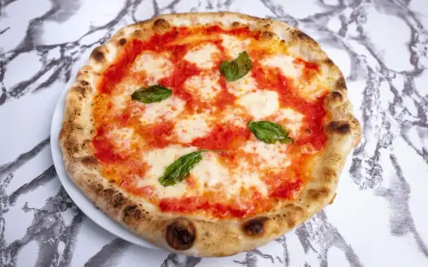 Pyszna pizza napoletana z pomidorami, mozzarellą i bazylią na białym talerzu, na tle marmurowego wzoru.