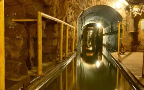 Podziemny tunel z wodą i żółtymi poręczami, idealny na zwiedzanie kopalni.