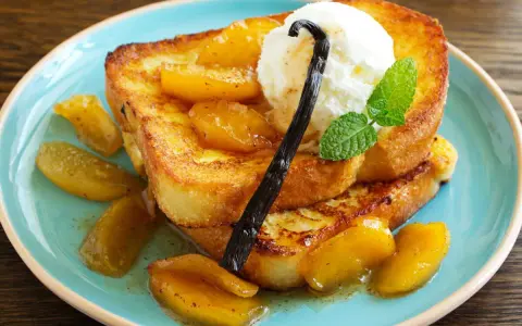Délicieux pain perdu brioché, garni de fruits caramélisés, d'une boule de glace à la vanille et d'une gousse de vanille.