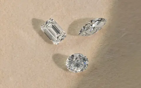 Tre diamanti di taglio diverso (smeraldo, marquise, rotondo) su sfondo chiaro, pronti per la classificazione diamanti.
