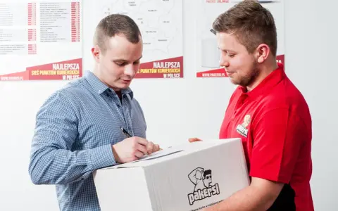 Kurier w czerwonej koszulce przekazuje paczkę, a klient podpisuje dokument. Zastanawiasz się, ile zarabia kurier?