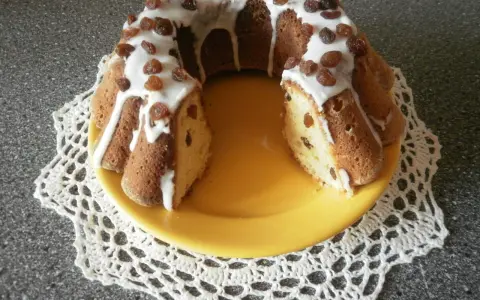 Pyszna babka drożdżowa z rodzynkami, polana lukrem i ozdobiona bakaliami, prezentuje się apetycznie na żółtym talerzu.