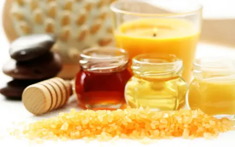 Ingredientes para un exfoliante corporal casero: sales, miel, aceites y una vela aromática.