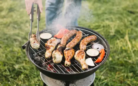 Rozpalanie grilla to sztuka! Na ruszcie skwierczą kiełbaski, kurczak i warzywa. Dym unosi się, zapowiadając pyszny posiłek.
