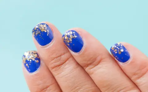 Dłoń z paznokciami w kolorze kobaltowym, ozdobionymi złotym brokatem. Stylizacja idealna dla każdej baby boomer z brokatem.