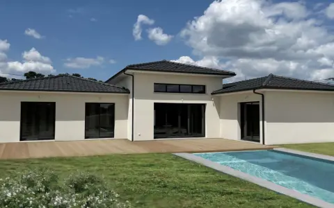 Une maison du sud moderne avec piscine, terrasse en bois et grand jardin sous un ciel bleu nuageux.