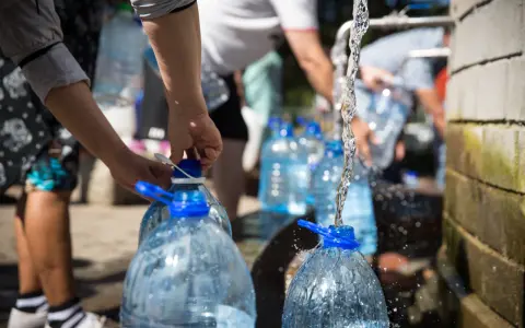 Menschen füllen Wasser in große Plastikflaschen. Die Frage, wie lange bleibt Wasser im Kanister frisch, ist hier relevant.