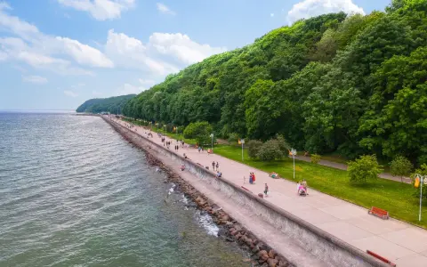 Spacer po molo południowym wzdłuż zielonego wybrzeża. Ludzie spacerują, odpoczywają na ławkach, ciesząc się pięknym dniem nad morzem.