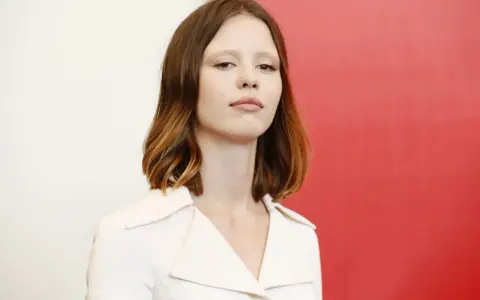 La giovane attrice protagonista del film di mia goth, con capelli castani mossi e un'espressione intensa, indossa un abito bianco.