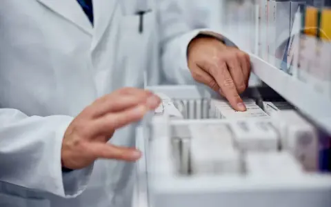 Farmaceuta szuka zamiennika leku Zarixa, przeglądając opakowania leków w aptece.