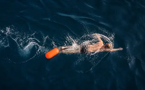 Un nageur profite d'une séance de nage en eau libre, suivi d'une bouée orange vif.