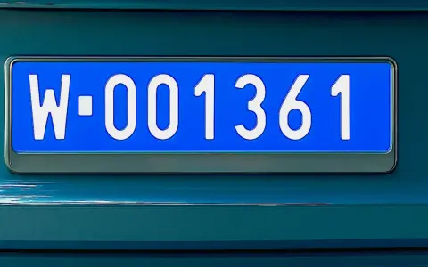 Niebieskie tablice rejestracyjne z numerem W-001361 na ciemnozielonym samochodzie.