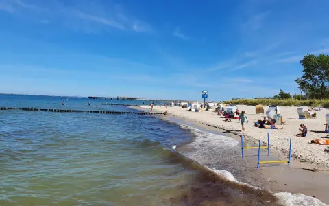 En solig tysk strand med folk som njuter av havet och sanden. En brygga sträcker sig ut i vattnet.