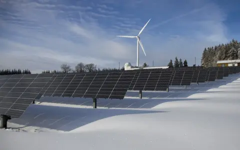 Panele fotowoltaiczne i wiatrak na tle zimowego krajobrazu. Rozliczenie z PGE za energię odnawialną.