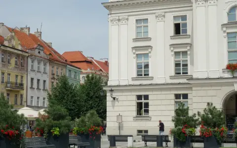 Urokliwe miasto nad Prosną z zabytkową architekturą, zielenią i ławkami w centrum.