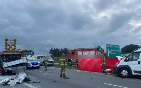 Miejsce wypadku kampera. Straż pożarna i policja zabezpieczają teren po zdarzeniu drogowym. Widoczny rozbity pojazd i czerwony namiot.