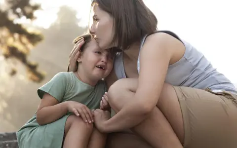 Madre consola la figlia che piange, un abbraccio che mostra le diverse tipologie di attaccamento sicuro e amorevole.