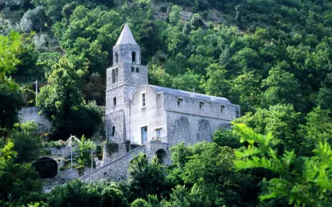 Antica chiesa in pietra su un fianco di montagna, circondata da alberi lussureggianti. I tramonti montagna qui sono magici.