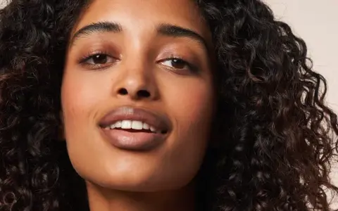Ein Porträt einer Frau mit voluminösen, dunklen Locken, die die Curly Girl Methode perfektioniert. Ihre Haut strahlt, ihre Augen funkeln.