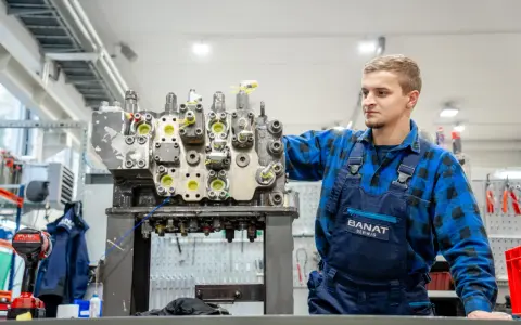 Mechanik w niebieskim kombinezonie pracuje nad budową rozdzielacza hydraulicznego w warsztacie.