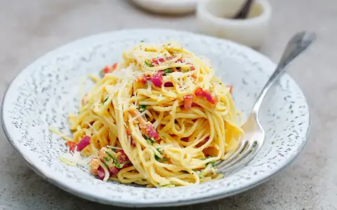 Pyszna carbonara ze śmietaną, okraszona boczkiem i parmezanem, czeka na widelcu.