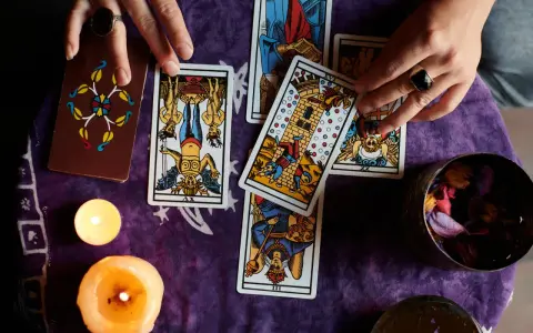 Manos de tarotista que es, barajando cartas y velas encendidas sobre tela morada.