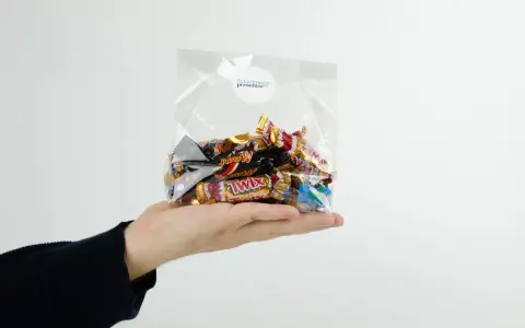 En hand håller en presentkorg i cellofan fylld med choklad.