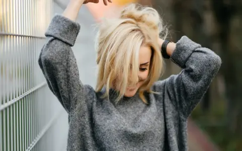 Blondynka w szarym swetrze, z włosami opadającymi na twarz. Marzy o gładkiej skórze, rozważa depilację laserową jasnych włosów.