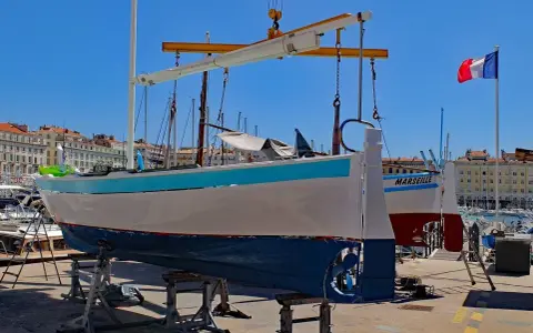 Un bateau hors de l'eau, prêt pour la maintenance, avec le nom "MARSEILLE" peint sur sa coque. Le drapeau français flotte au loin.