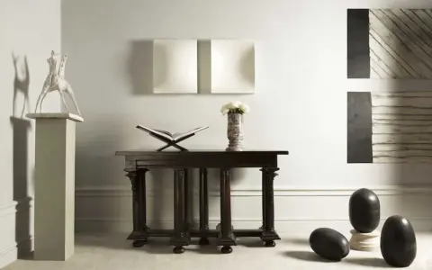 En elegant inredning med en skulptur av Claes Dahlen, en öppen bok, blommor i en vas och mörka stenägg.