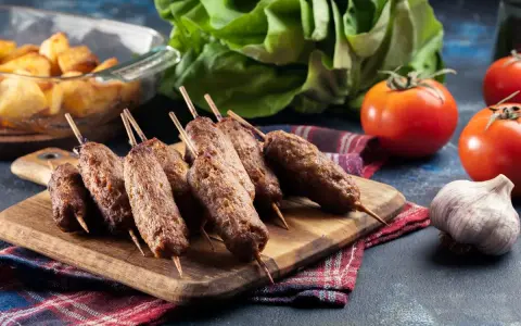 Aksamitne ćevapi na drewnianej desce, obok pomidory, czosnek i pieczone ziemniaki. Pyszny posiłek gotowy do podania.