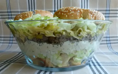 Warstwowa sałatka big mac w szklanej misie, z bułkami na wierzchu.