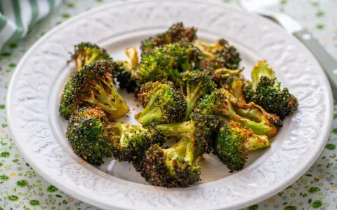 Brocoli en airfryer, crujiente y dorado, servido en un plato blanco con un mantel verde.