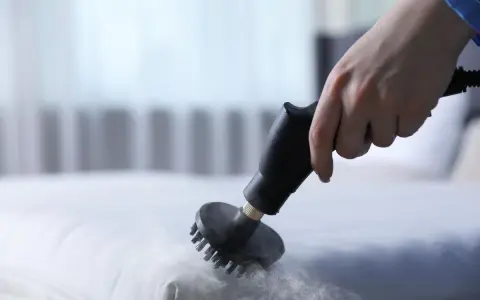 Main d'une personne utilisant un nettoyeur vapeur pour nettoyer un matelas en mousse. Une méthode efficace pour savoir comment nettoyer un matelas en mousse.