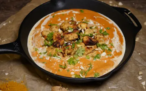 Ein authentisches Butter Chicken Rezept original in einer Gusseisenpfanne, garniert mit Koriander und gehackten Mandeln.