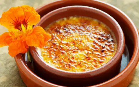 Crema catalana con una flor naranja. El postre tiene una capa de azúcar caramelizado crujiente.