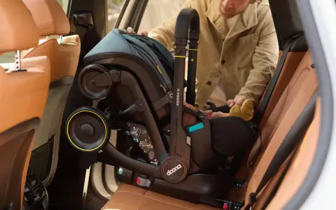 Mężczyzna wyjmuje fotelik z isofix z samochodu. Widać uchwyt i koła fotelika.