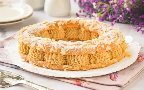 Un delicioso praliné que es un pastel Paris-Brest, cubierto de almendras laminadas y espolvoreado con azúcar glas.