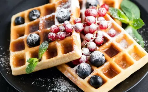 Keto gofry z mąki kokosowej z borówkami, porzeczkami i miętą, posypane cukrem pudrem.