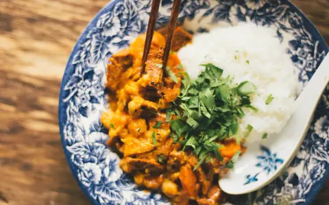 Miseczka z ryżem i curry, podana z posiekaną natką pietruszki, jedzona pałeczkami.