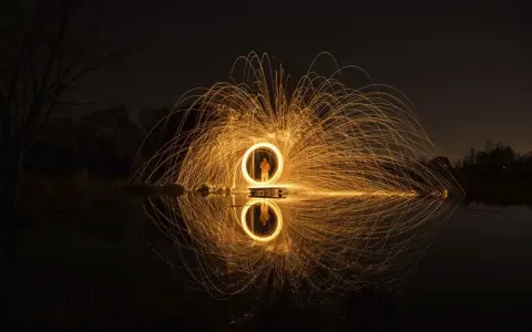 Un cerchio di scintille dorate, un uomo al centro, riflette sull'acqua. Un'opera d'arte che sembra **disegnare con la luce** nel buio della notte.