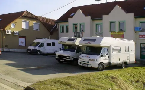 Trzy białe kampery zaparkowane przed budynkami z szyldami.