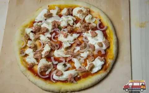 Gotowa do pieczenia pizza z tuńczykiem, mozzarellą i cebulą na drewnianej desce.