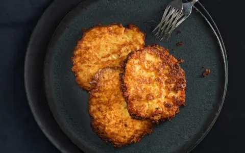 Drei goldbraune Kartoffelpuffer, frisch zubereitet im Thermomix, liegen auf einem dunklen Teller.