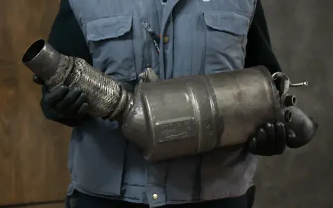 Mechanik w rękawiczkach trzyma zużyty element układu wydechowego, prawdopodobnie po problemach z wypalaniem DPF.