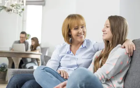 Madre e figlia sorridono, un momento di complicità che contrasta con il distacco emotivo dai figli in lontananza.