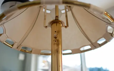 Detaljbild av en golvlampa i mässing från Ateljé Lyktan. Skärmen är av tyg med mässingsdetaljer.