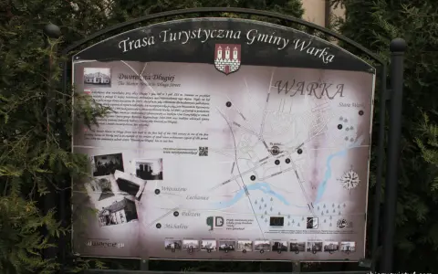 Mapa turystyczna gminy Warka z zaznaczonymi zabytkami, w tym Dworkiem na Długiej. W tle drzewa, a na dole strony logo "Warka" i adres strony.